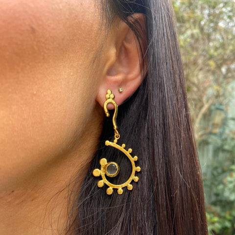 girl dark hair wearing gold  swirl drop earrings with  mauve stone